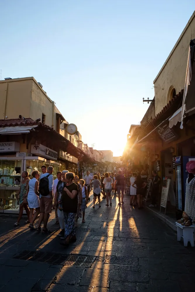 Shoppers on a stone street at sunset, long shadows thrown toward the camera