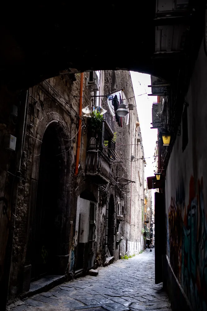 A Naples side street seen from under a dark arch, balconies and washing lines above the cobbles