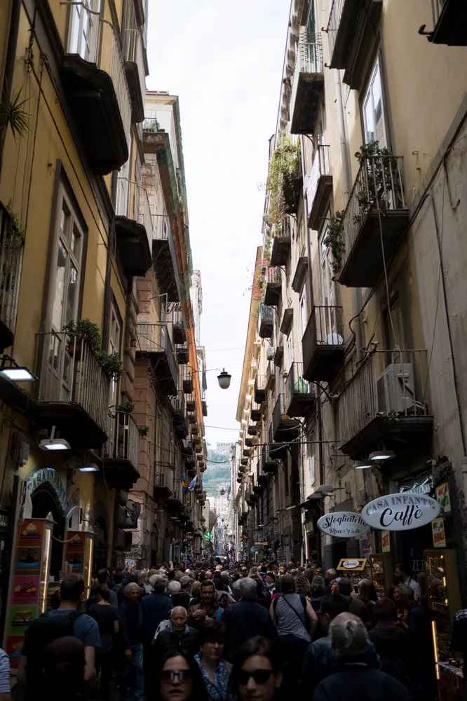 A crowded Naples street packed shoulder to shoulder between tall balconied buildings