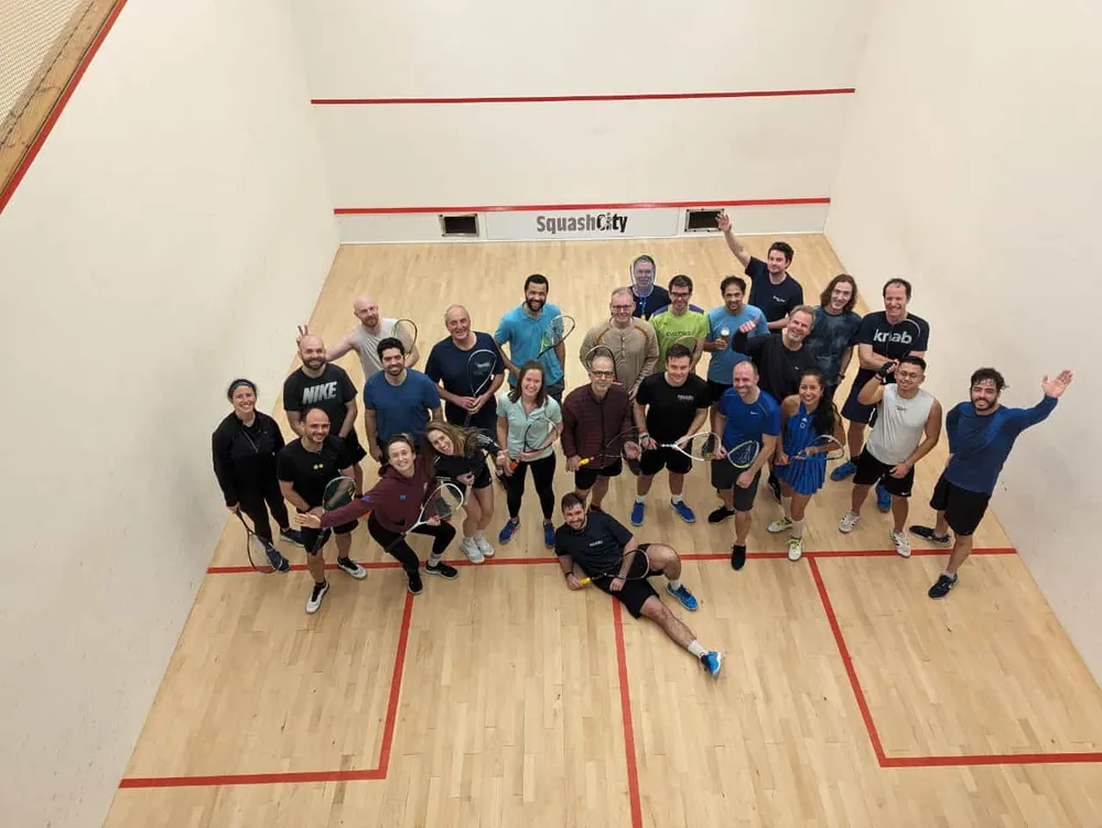 A large group of players gathered on court with their rackets, looking up at the camera