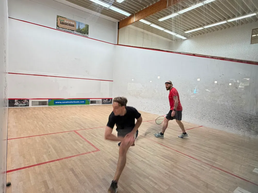A player lunging low to reach the ball while his opponent watches from behind