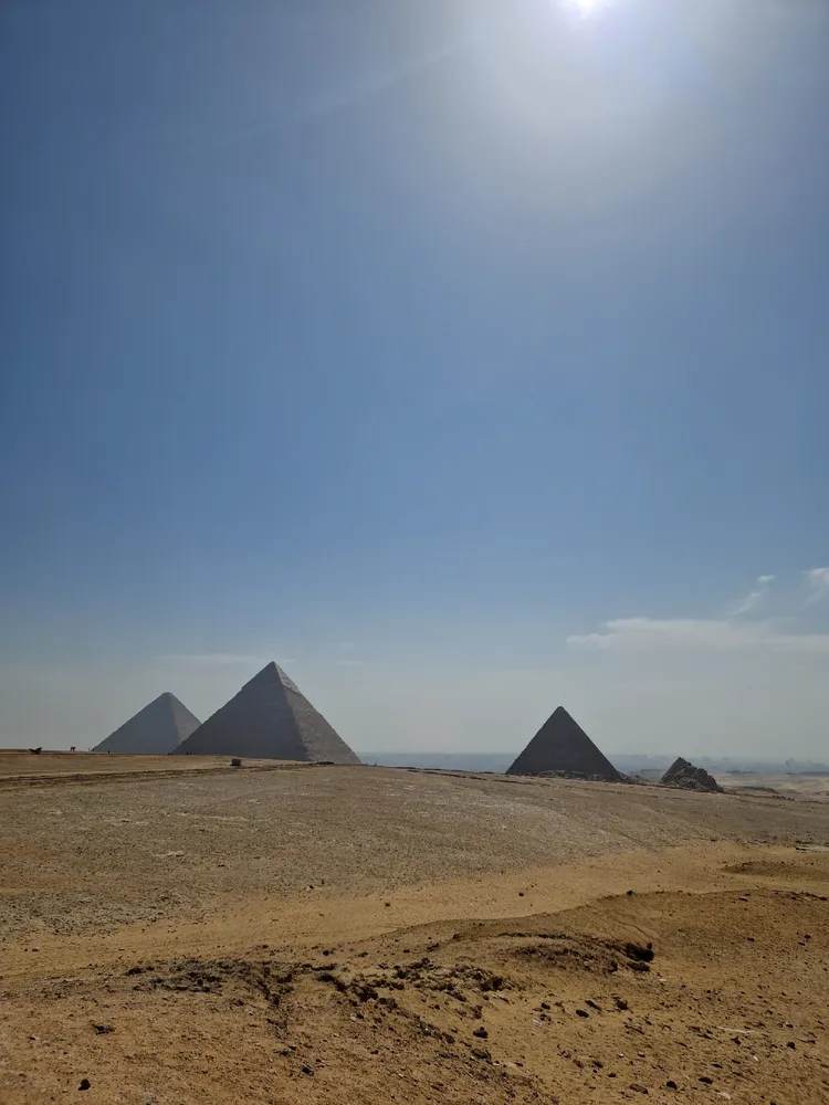 The pyramids at Giza rising from open desert under a bright hazy sky