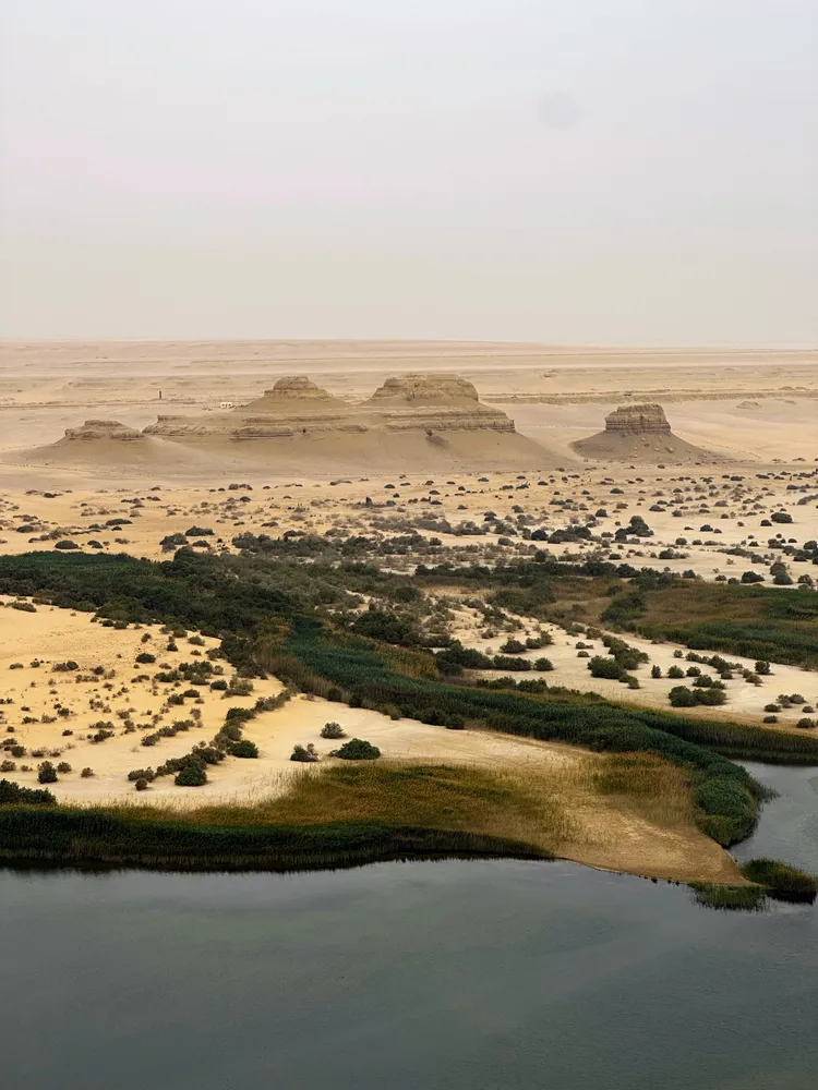 Sandstone buttes standing over a green oasis and lake in the Egyptian desert
